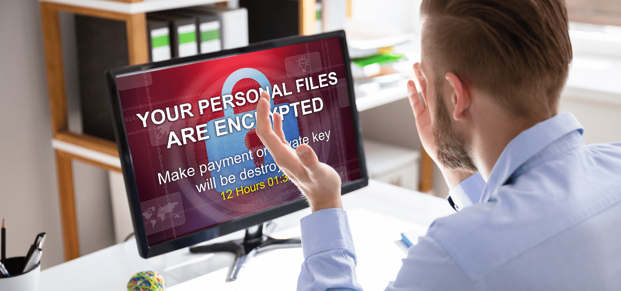 Computer screen showing a ransomware message as a person sits at a desk facing the monitor.