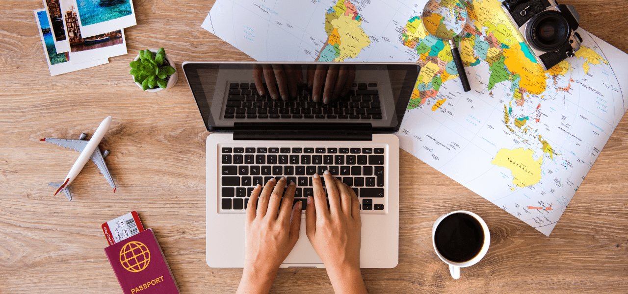 A person using a laptop on a table with travel photos and the world map.