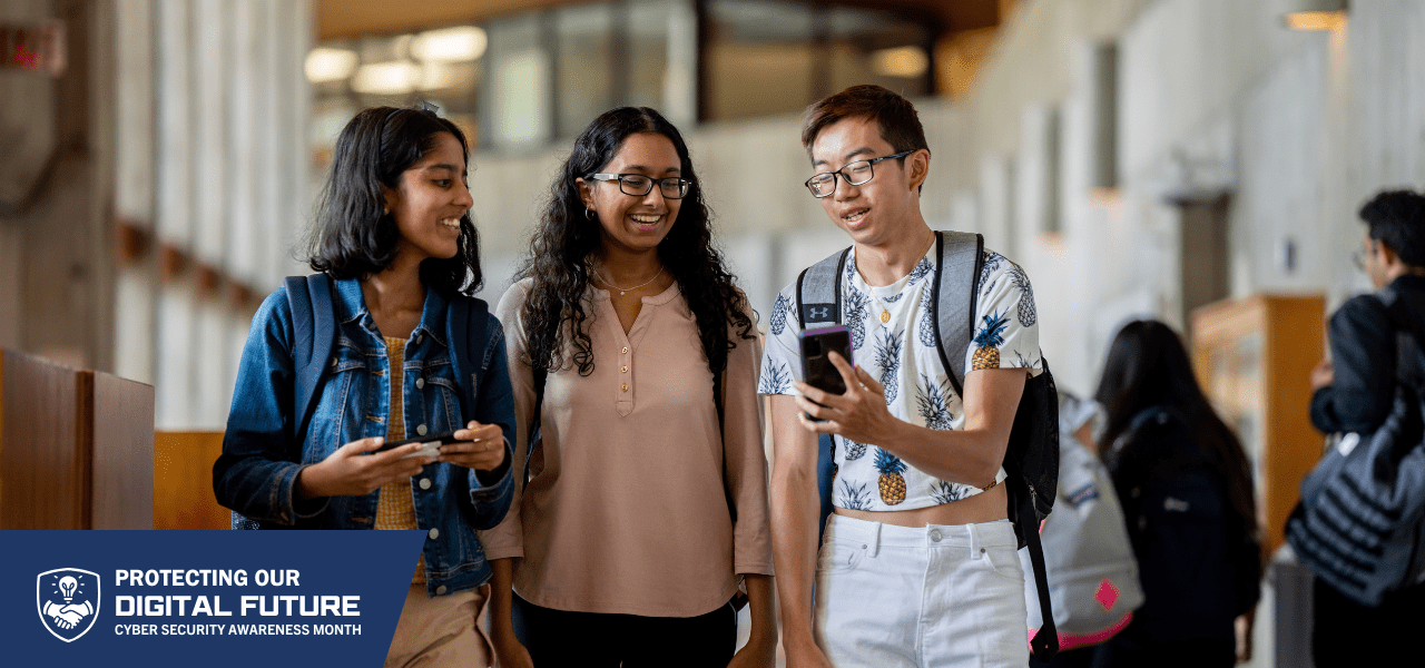 Three students walking together in a hallway, holding smartphones and wearing casual clothing with backpacks.