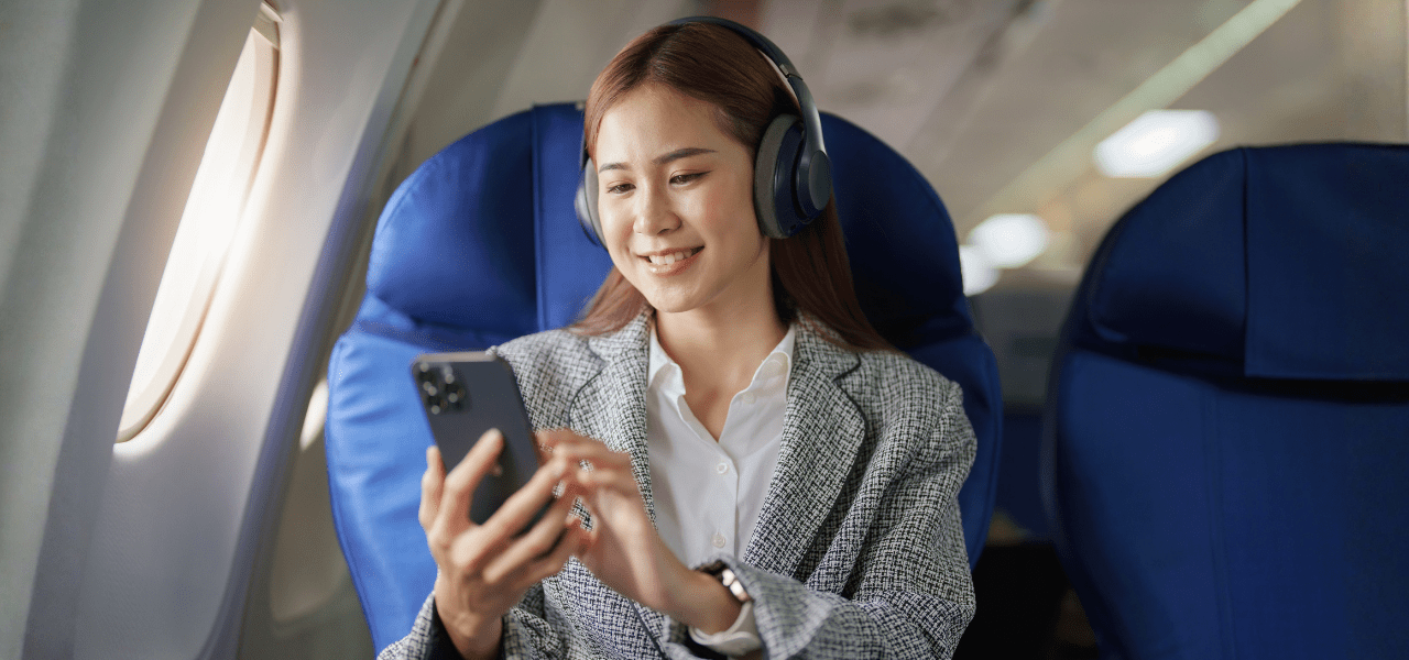 Person sitting on an airplane wearing headphones and using a smartphone.