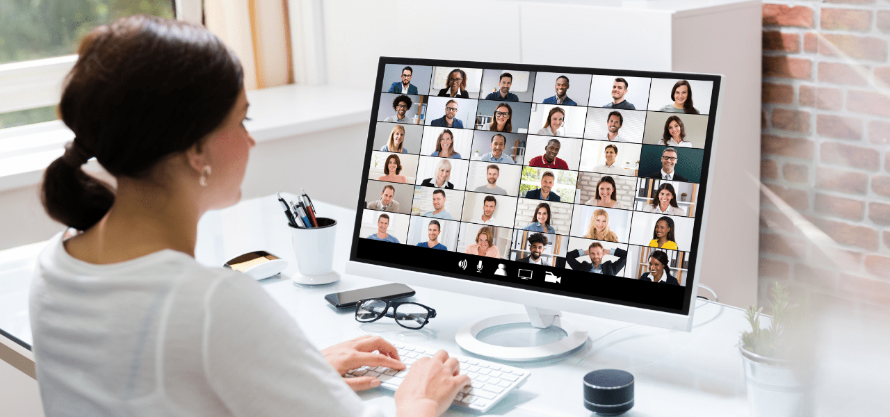 Person sitting at a desk using a computer displaying a large video conference with many participants in a grid layout.